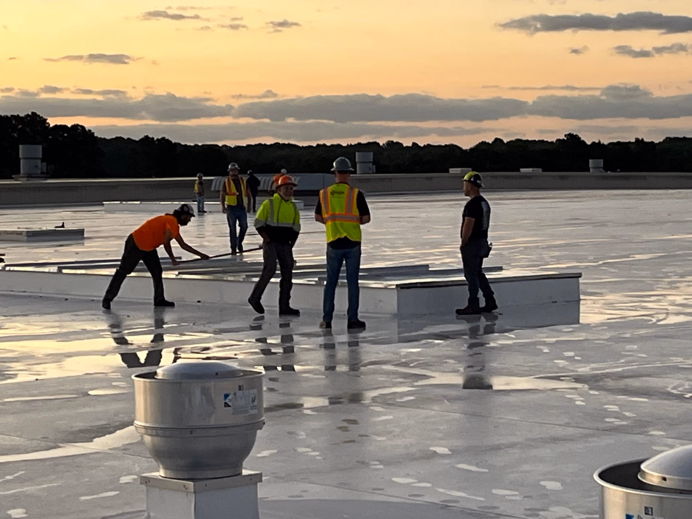 A PS&M safety supervisor briefing a roofing crew at first light on a commercial flat roof
