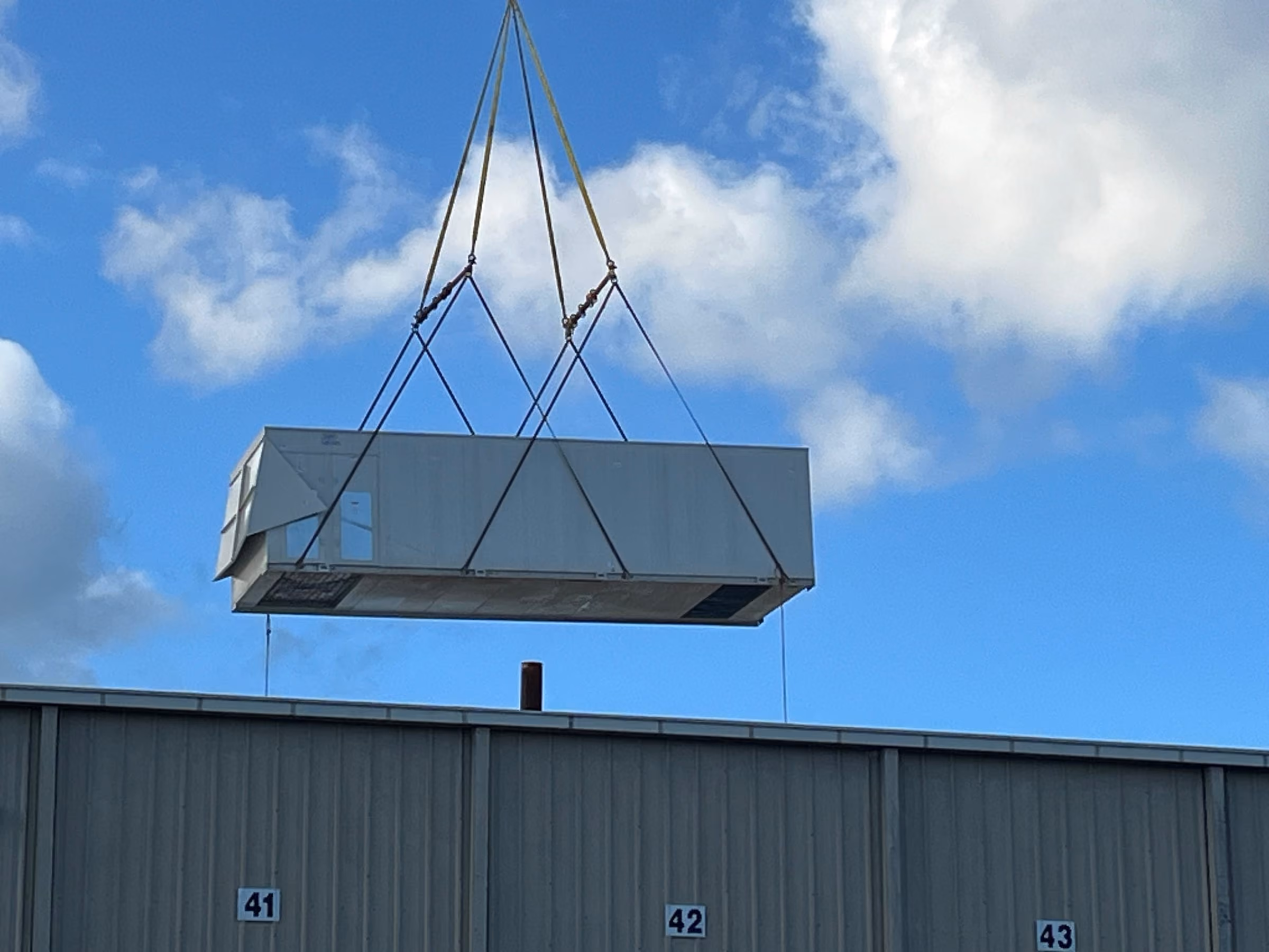 A rooftop air handling unit flown into position on rigging slings beneath a crane
